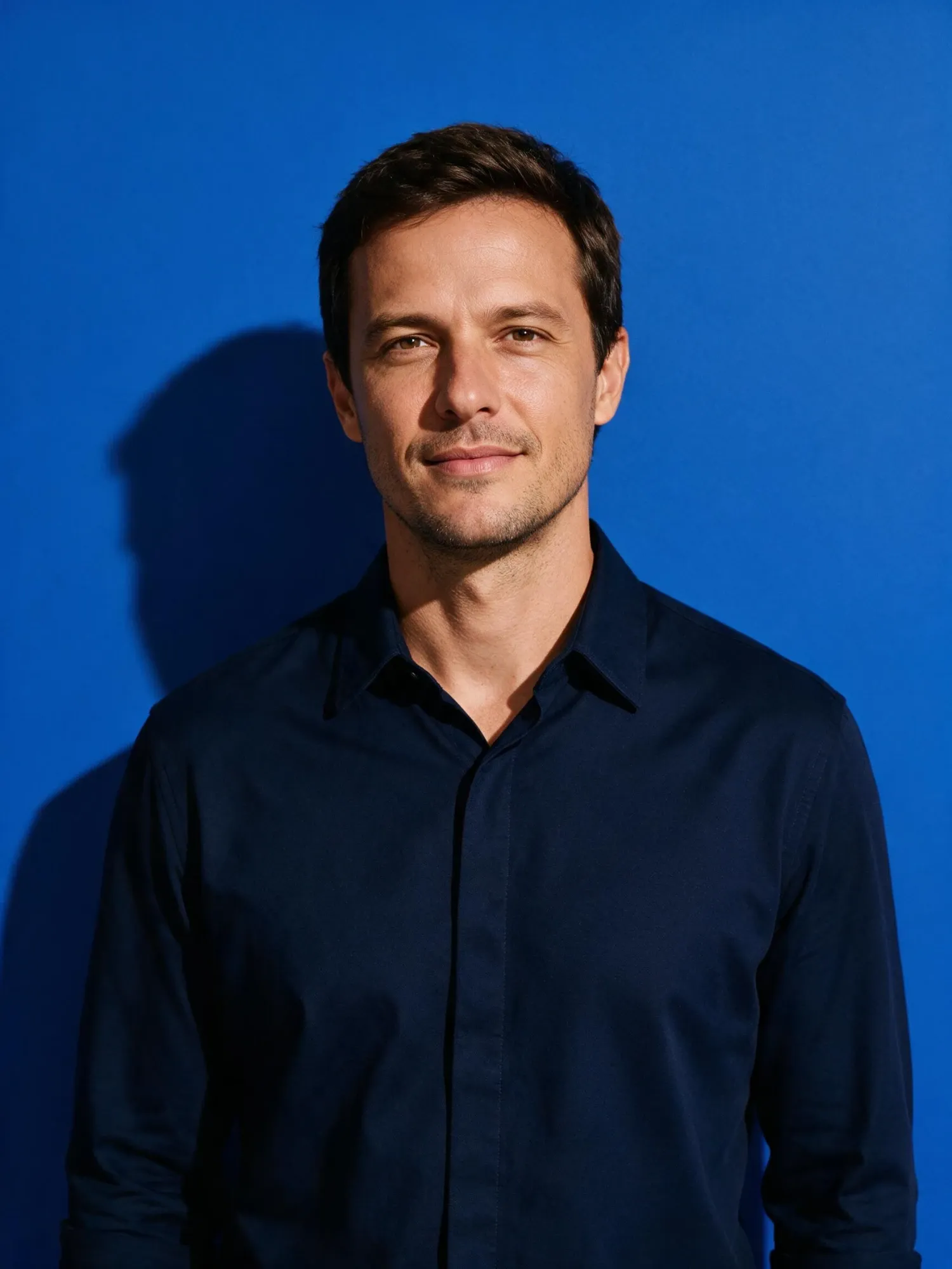 Homem de camisa azul-marinho diante de um fundo azul.